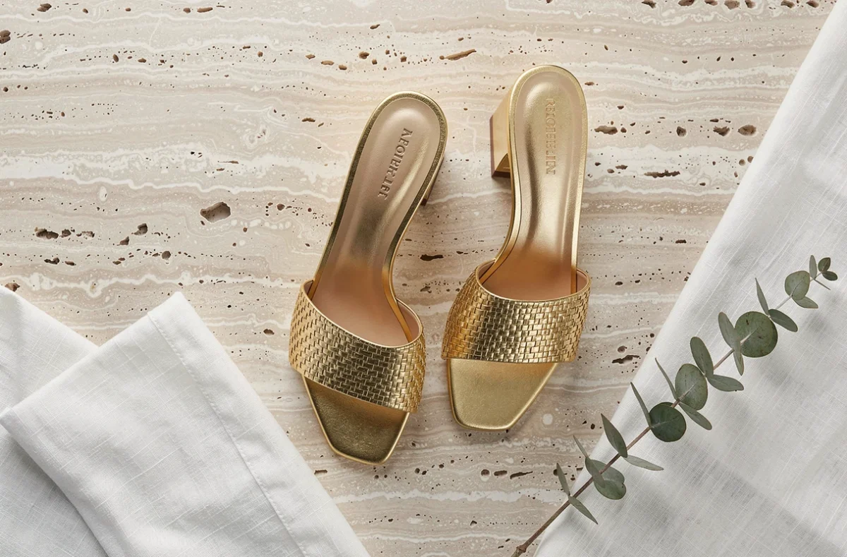 Paire de sandales dorées à petit talon sur surface en travertin avec accessoires de style, vue de dessus flat-lay mode et élégance féminine